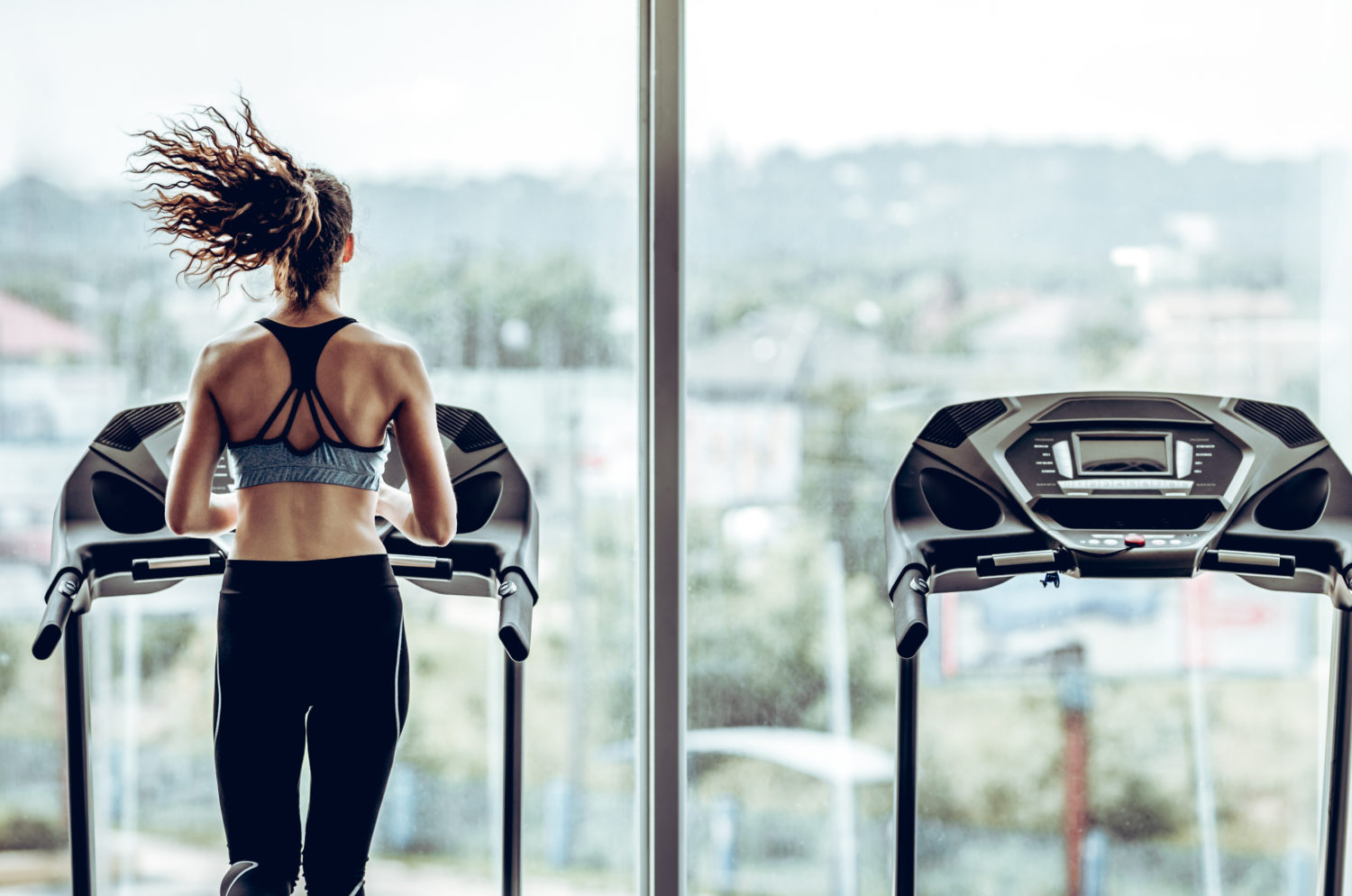 Attractive woman running on treadmill in sport gym, sport life and sport equipment. Back view.